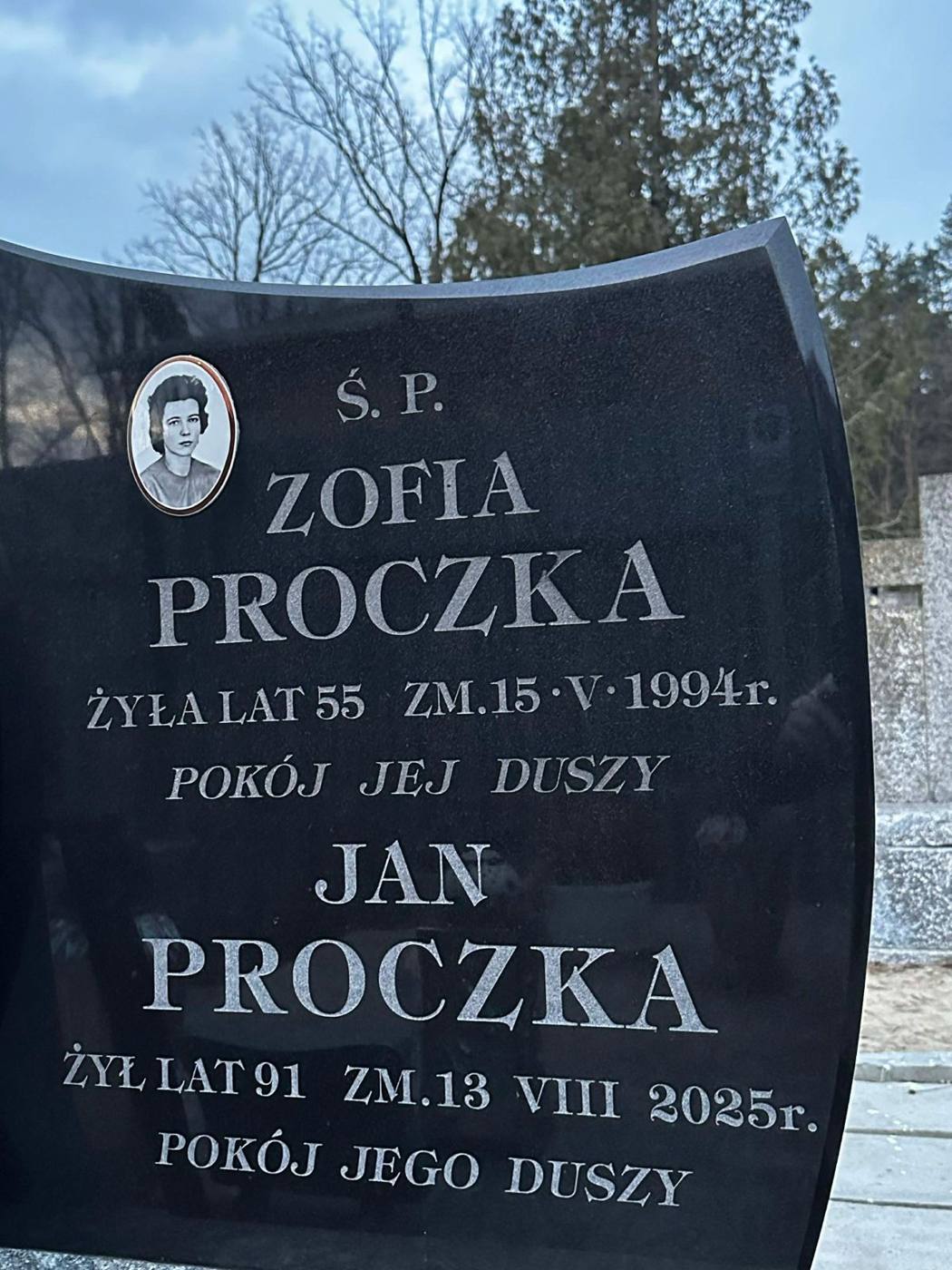 Czarny nagrobek z piaskowaną napisem Zofii i Jana Proczków oraz owalnym zdjęciem